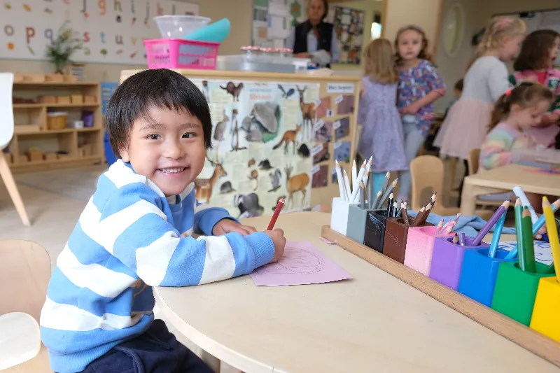 child at table with work and smiling at the camera
